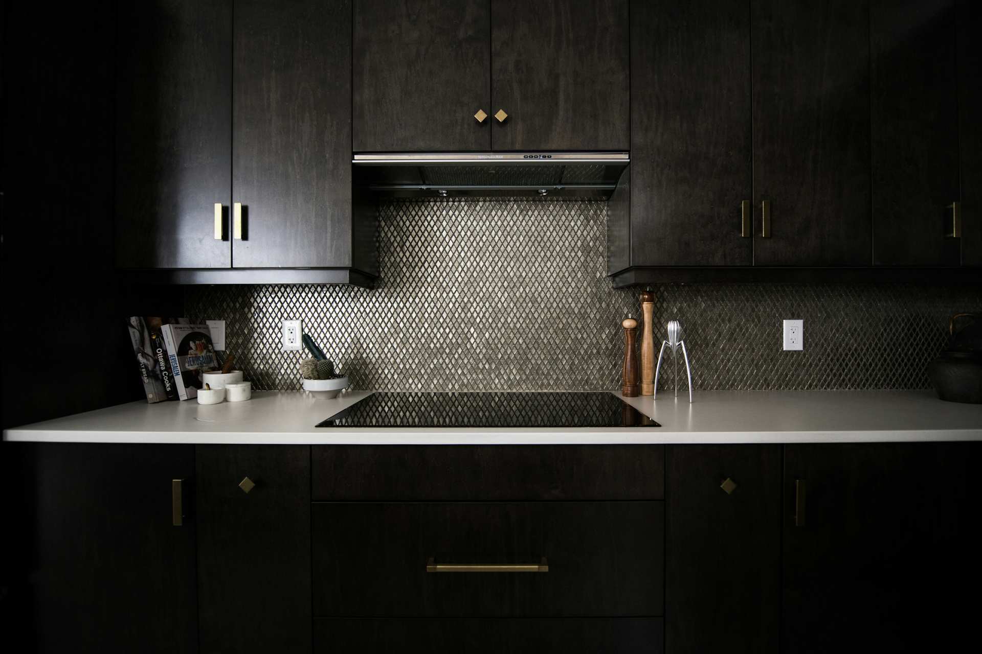 Dark kitchen with an integrated cooktop and tall stone backsplash