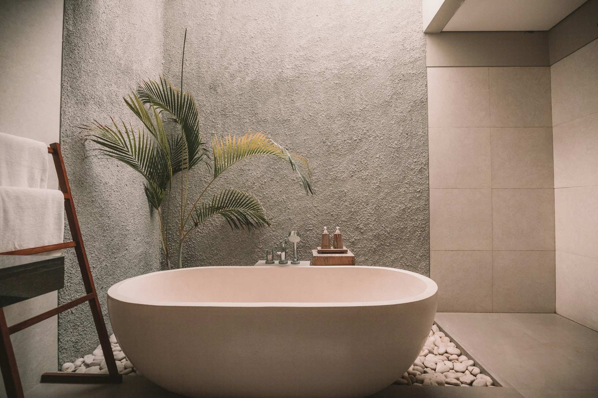 Freestanding stone bathtub beside a textured plaster wall and river-stone floor