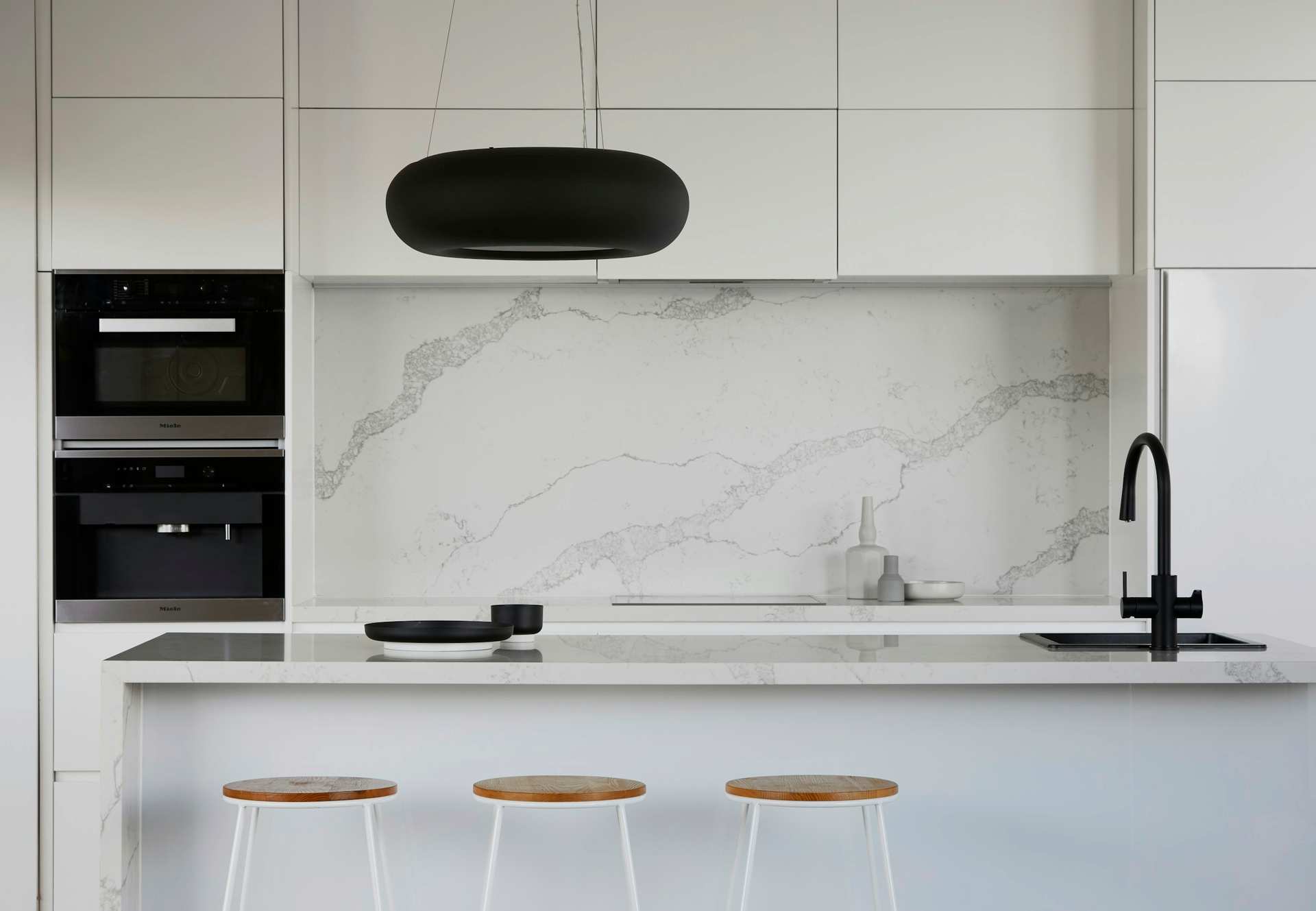 White kitchen with a marble backsplash, integrated ovens and a matte black faucet