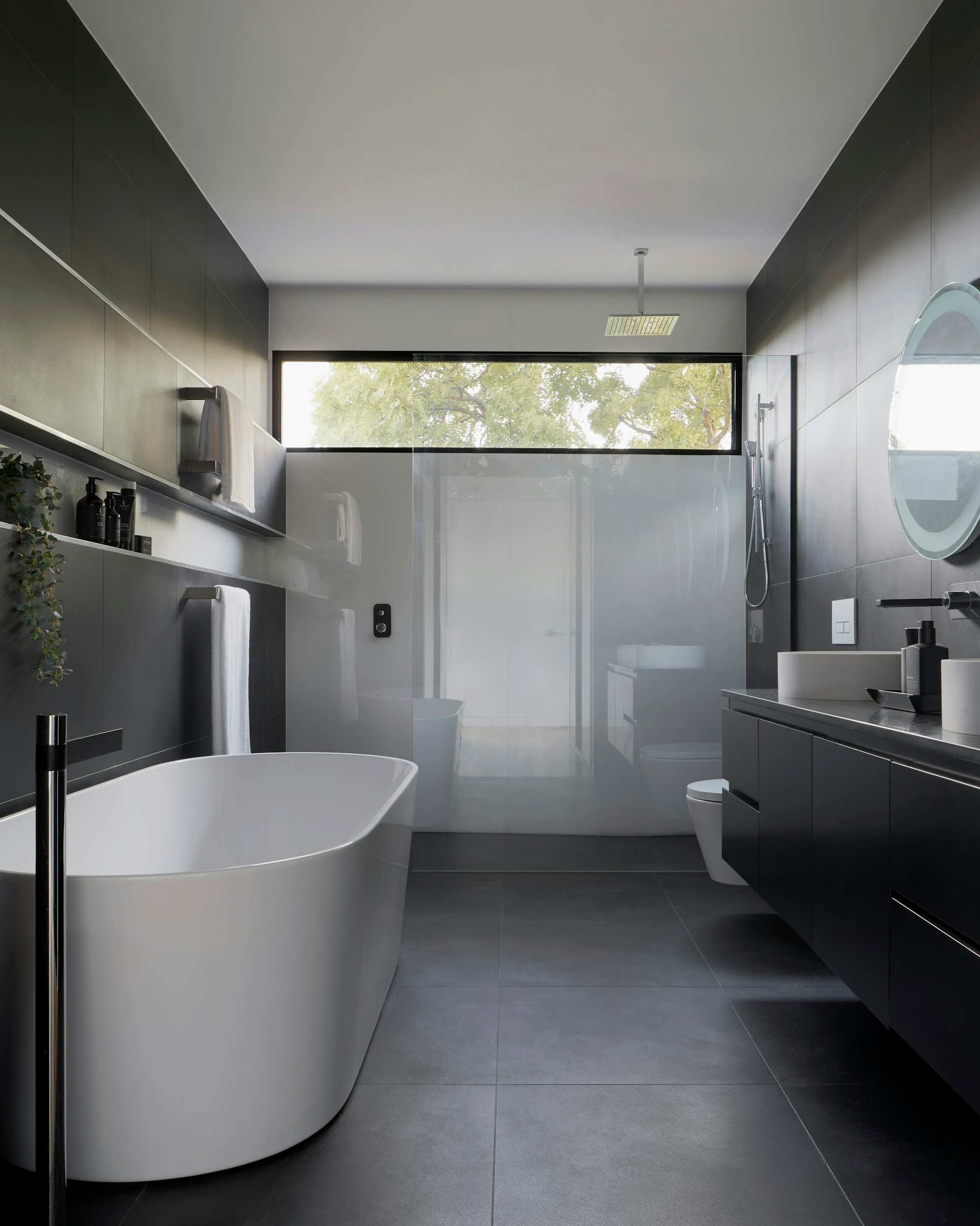 Dark stone bathroom with a freestanding tub under a clerestory window